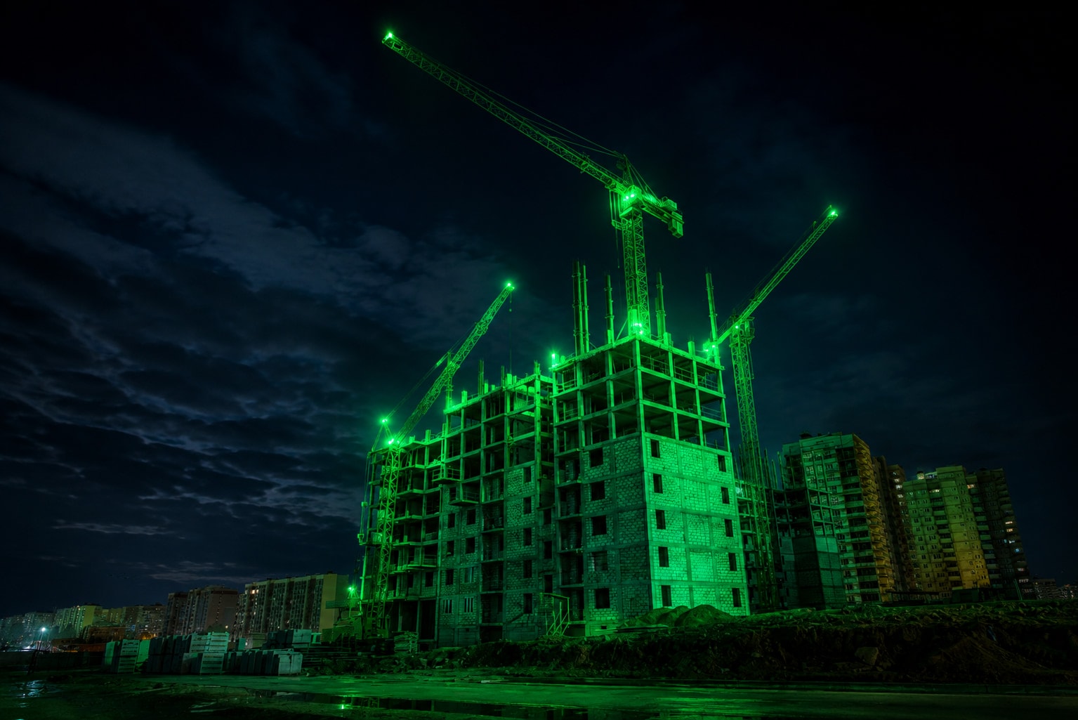 Tower cranes over a residential block under construction at night