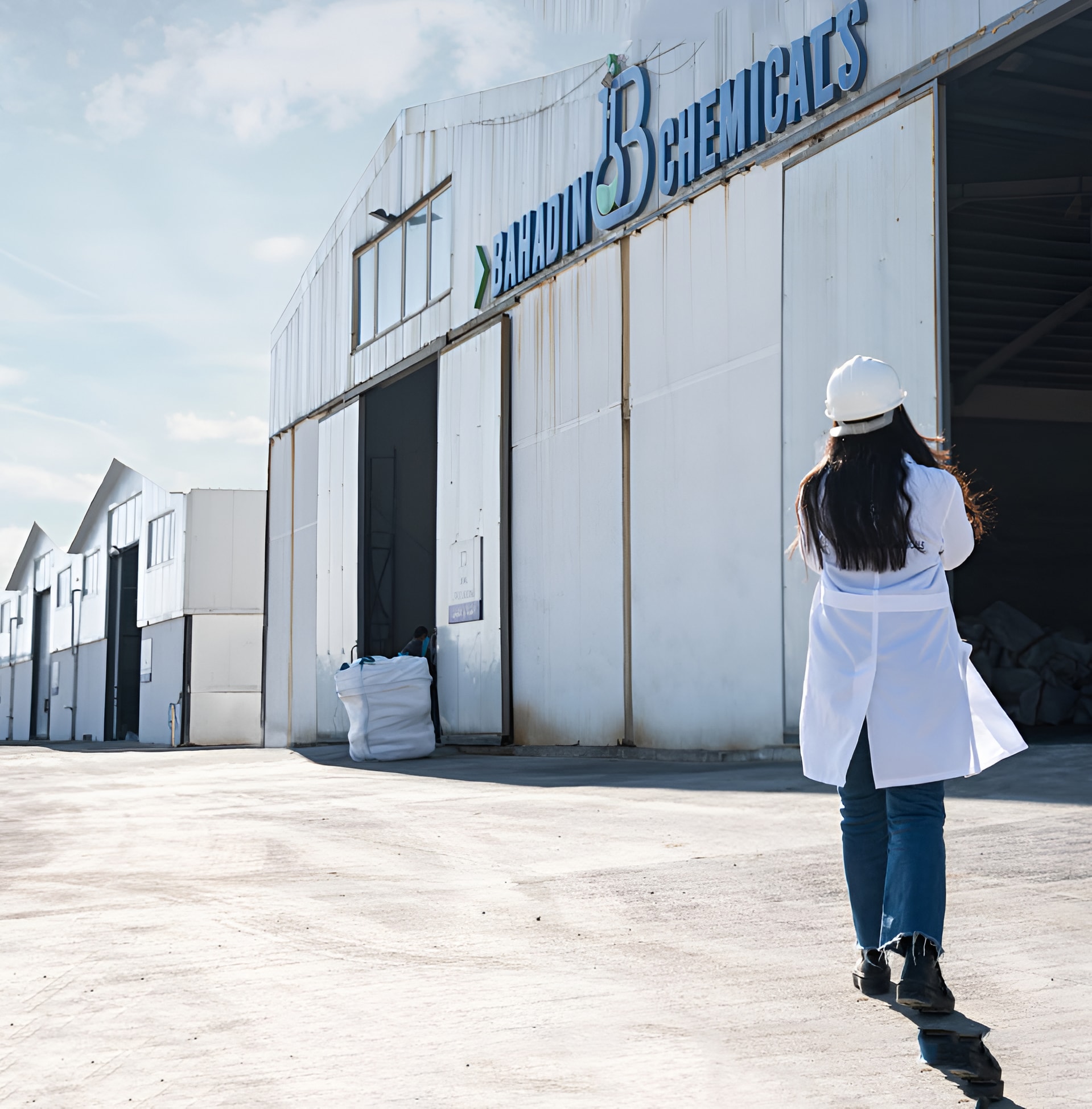 A chemist in a lab coat and hard hat walking to the Bahadin Chemicals plant