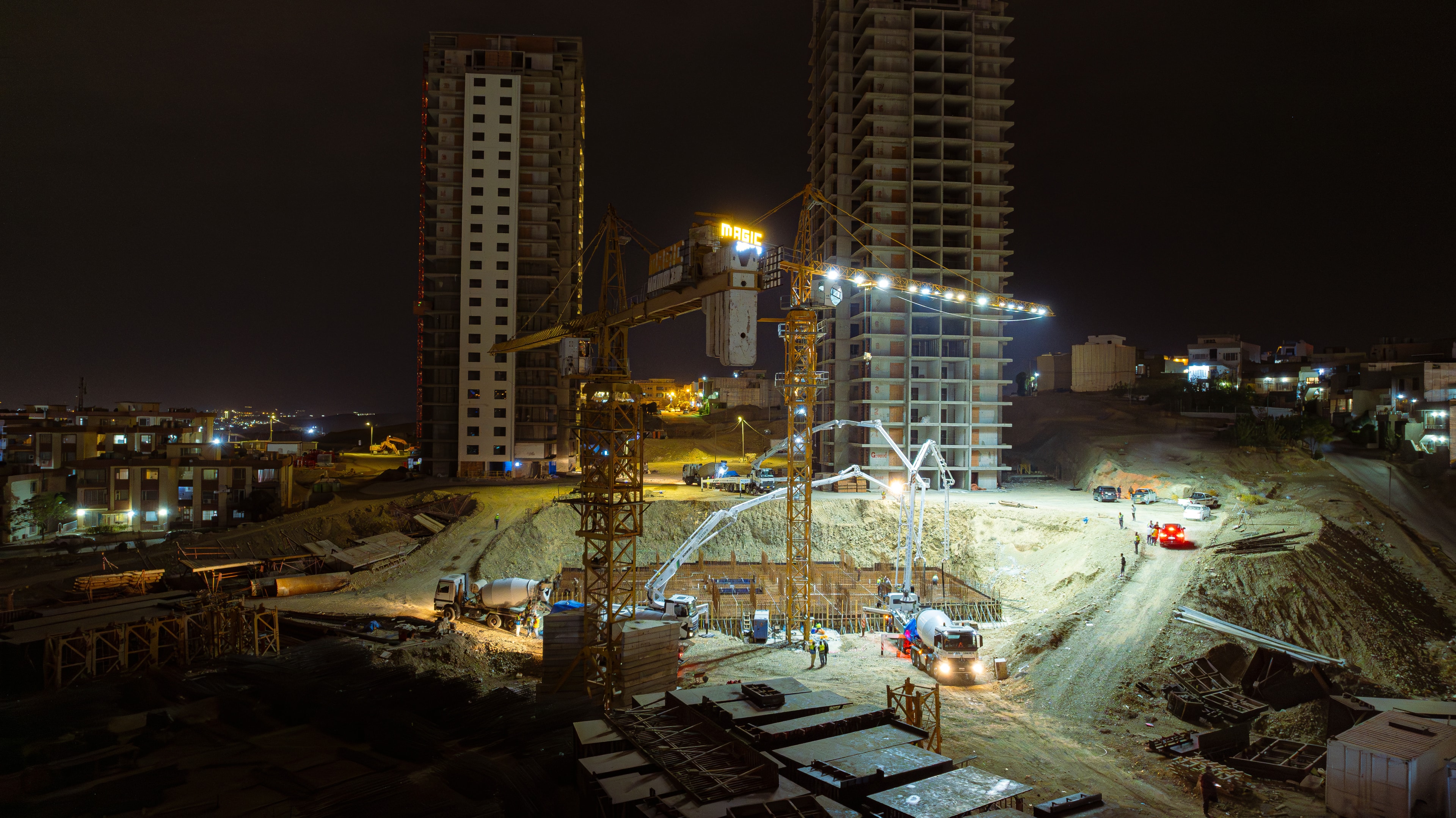 A tower under construction at night, a concrete pump and mixer trucks working under floodlights